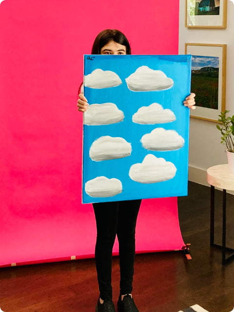 Little girl with dark hair holding a blue sky with white cloud painting on unframed canvas